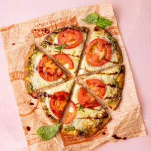 Naan pesto pizza with sliced tomatoes and balsamic glaze garnished with fresh basil.