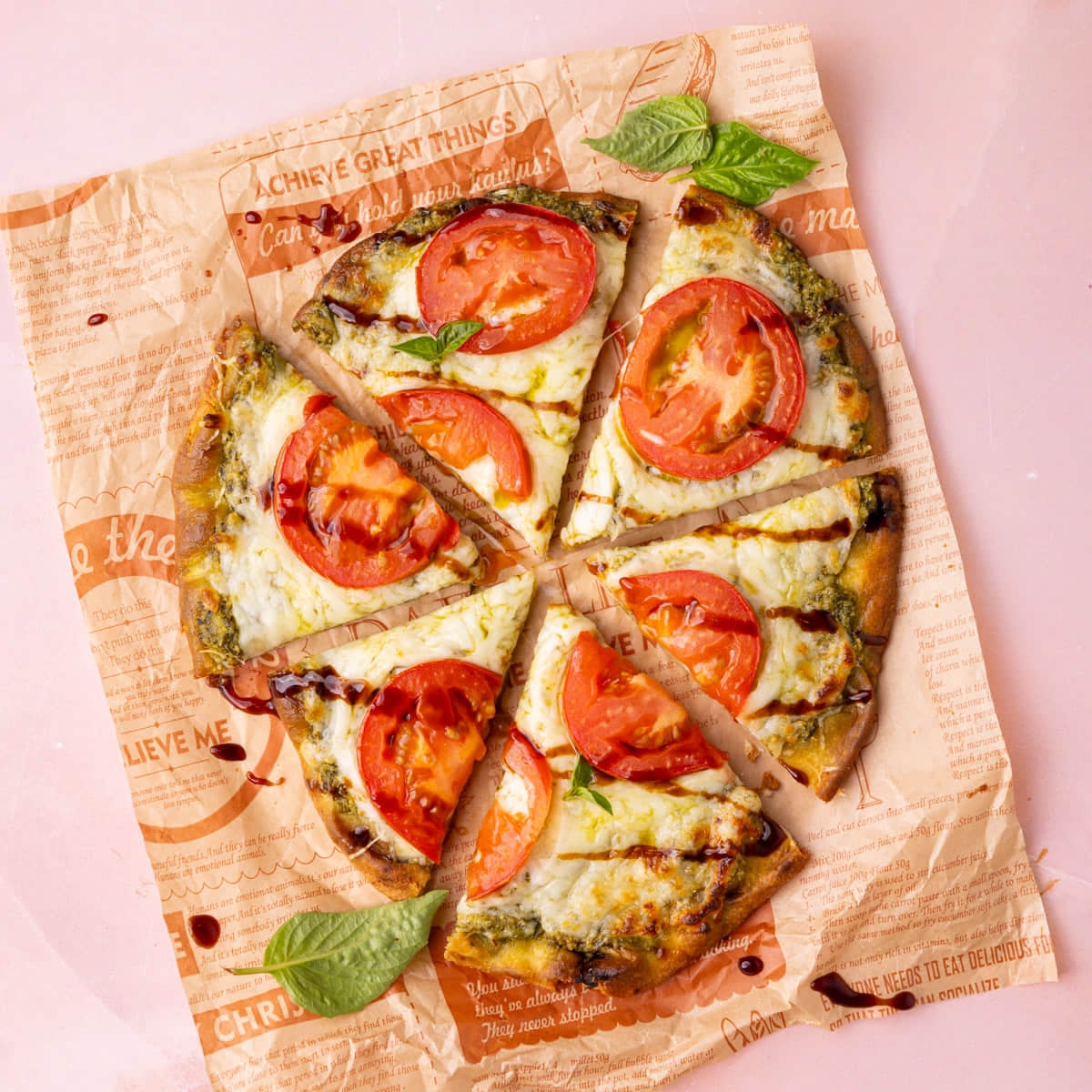 Naan pesto pizza with sliced tomatoes and balsamic glaze garnished with fresh basil.