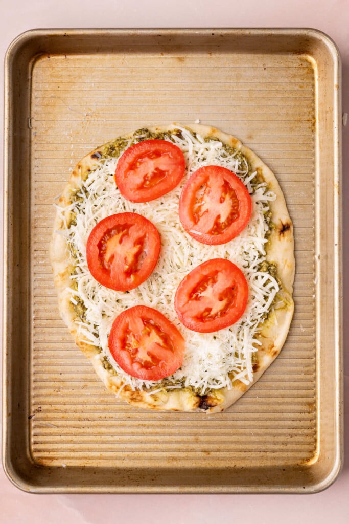 Fresh sliced tomatoes on top of pesto naan pizza, ready for the oven.