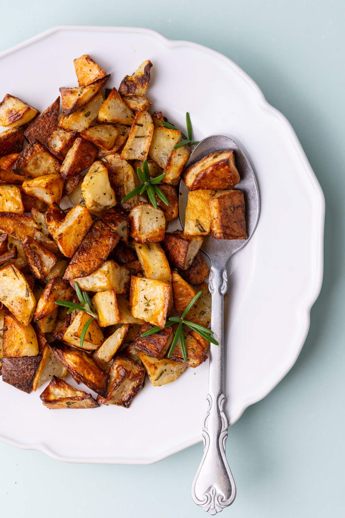 Overhead image of white plate with crispy breakfast potato finished with fresh rosemary.