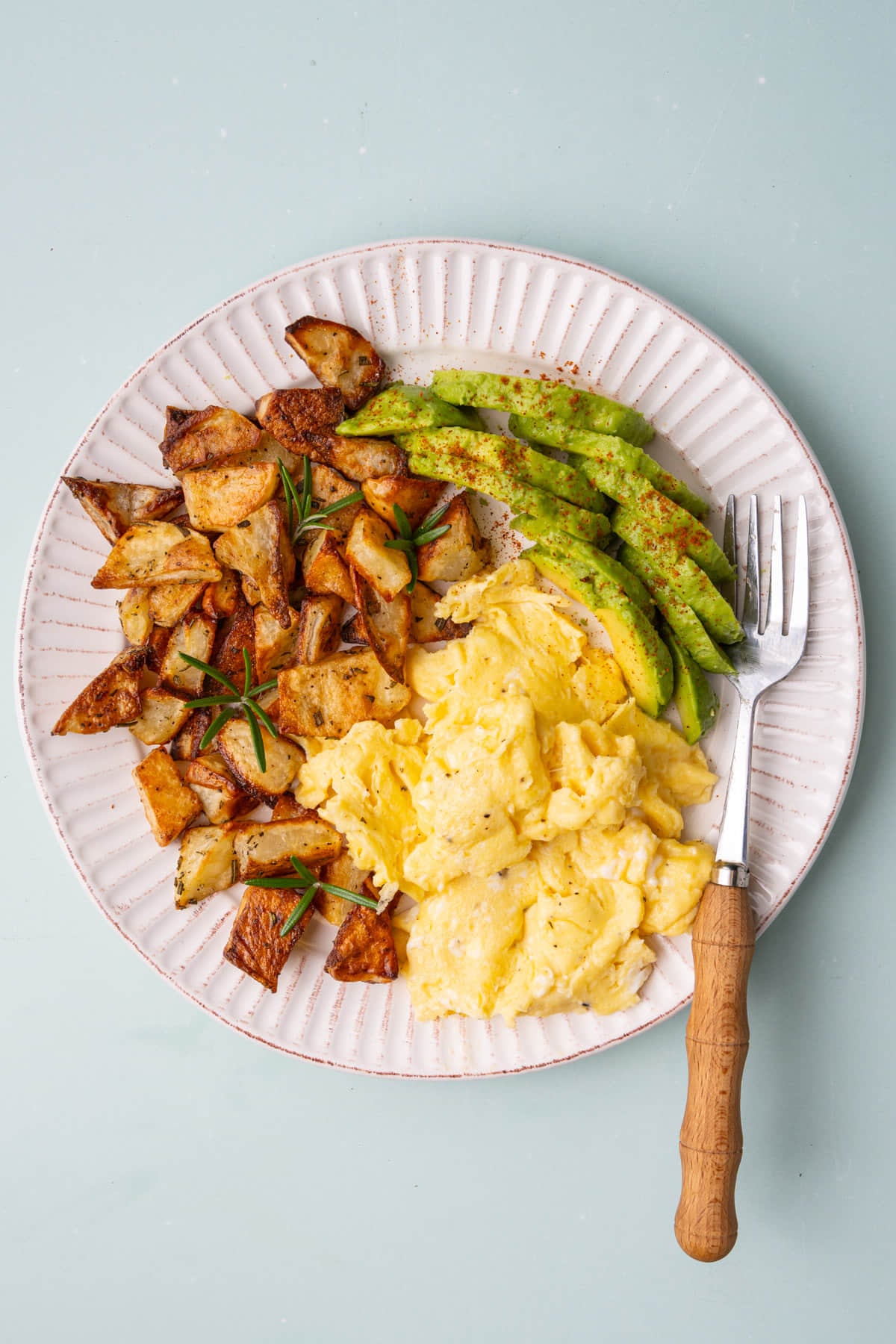 Crispy roasted breakfast potatoes plated with scrambled eggs and sliced avocado.