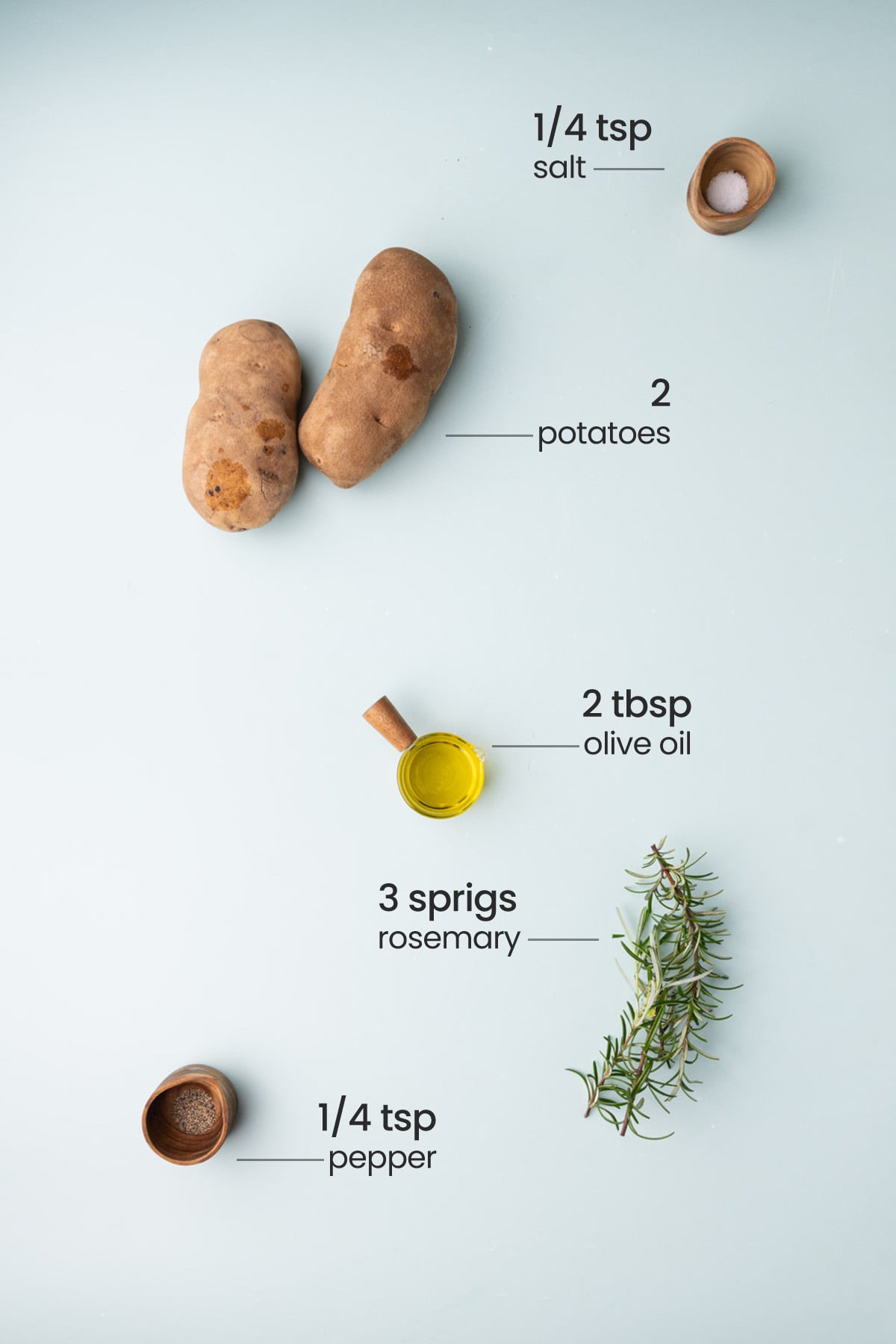 Overhead view of the ingredients for breakfast potatoes - salt, potatoes, olive oil, rosemary, and pepper.