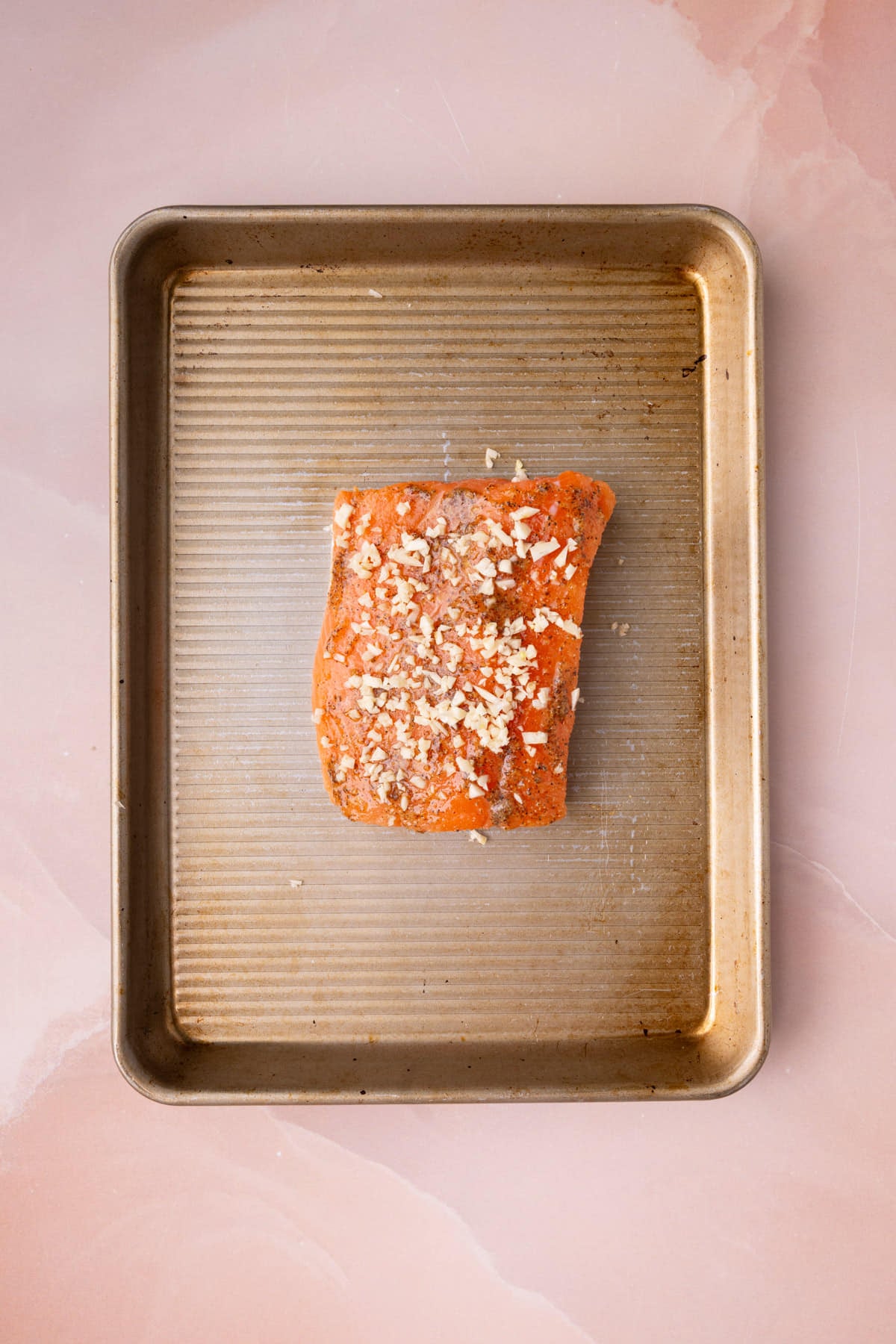 Minced garlic on top of honey mustard salmon prepped and ready for the oven.