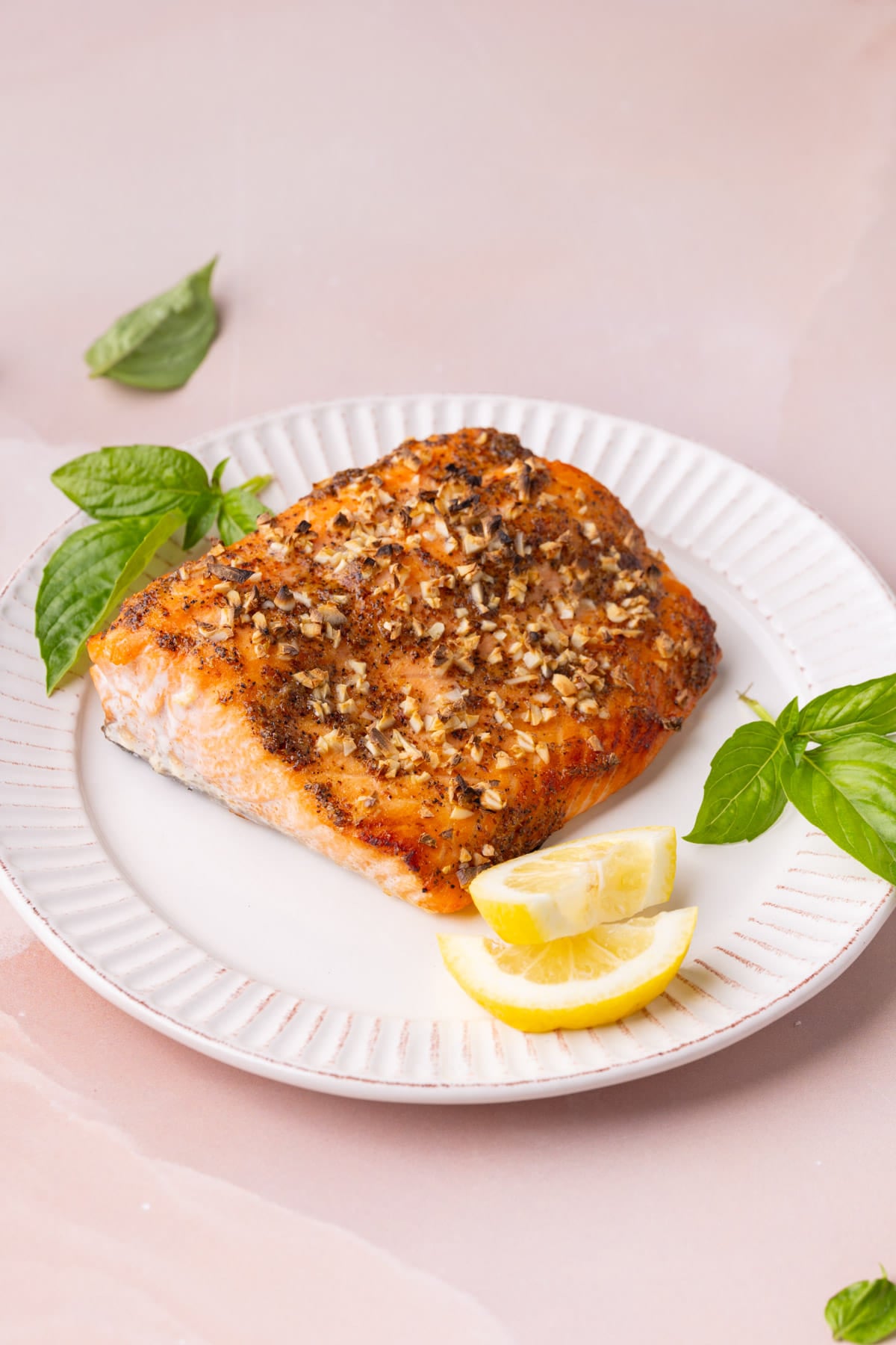 Roasted salmon with honey and mustard topped with garlic and plated with fresh basil and lemon wedges.