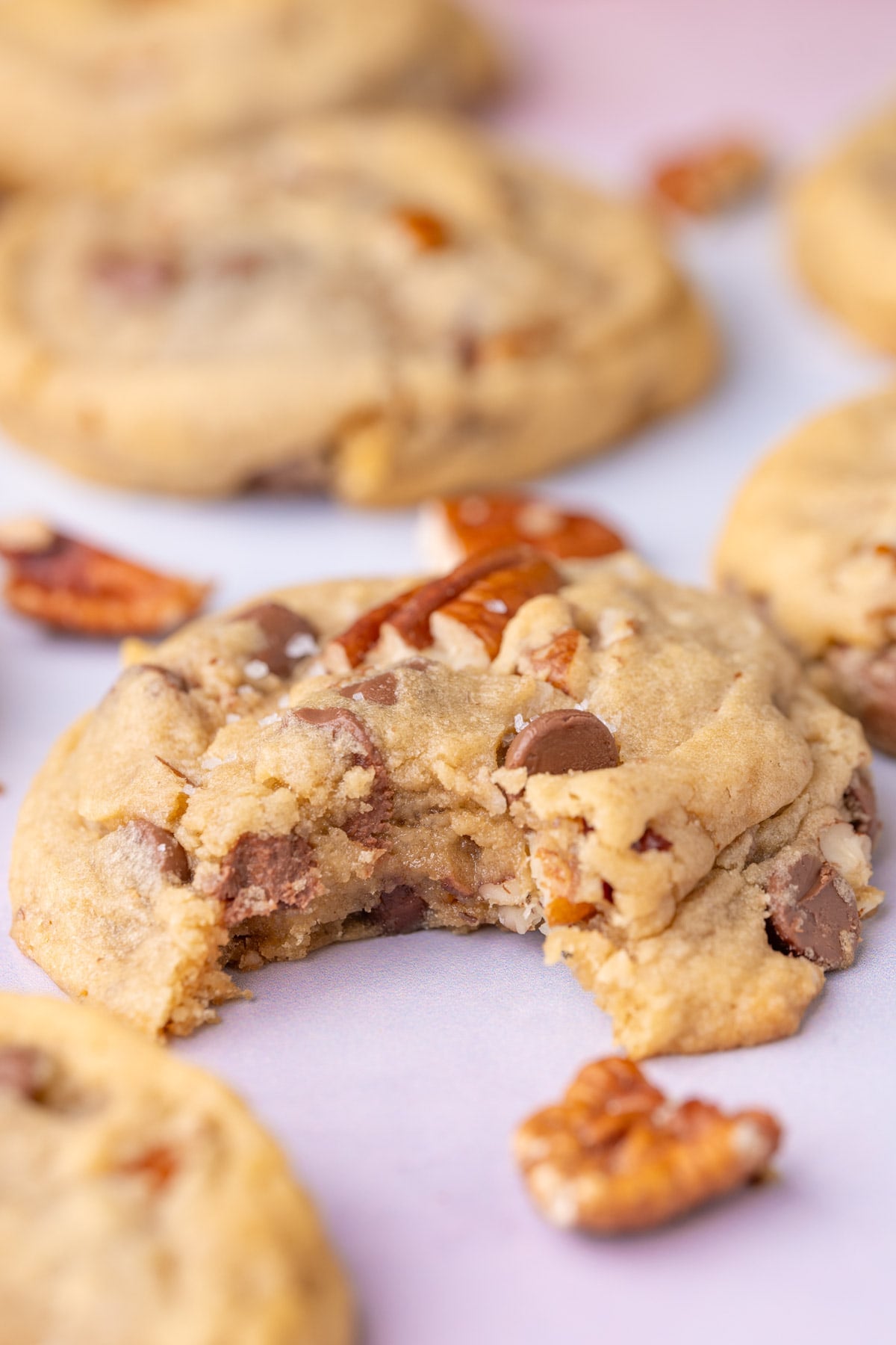Close up of chocolate chip cookie with pecans with a bite taken out of it so you can see the inside and outside of the cookie.