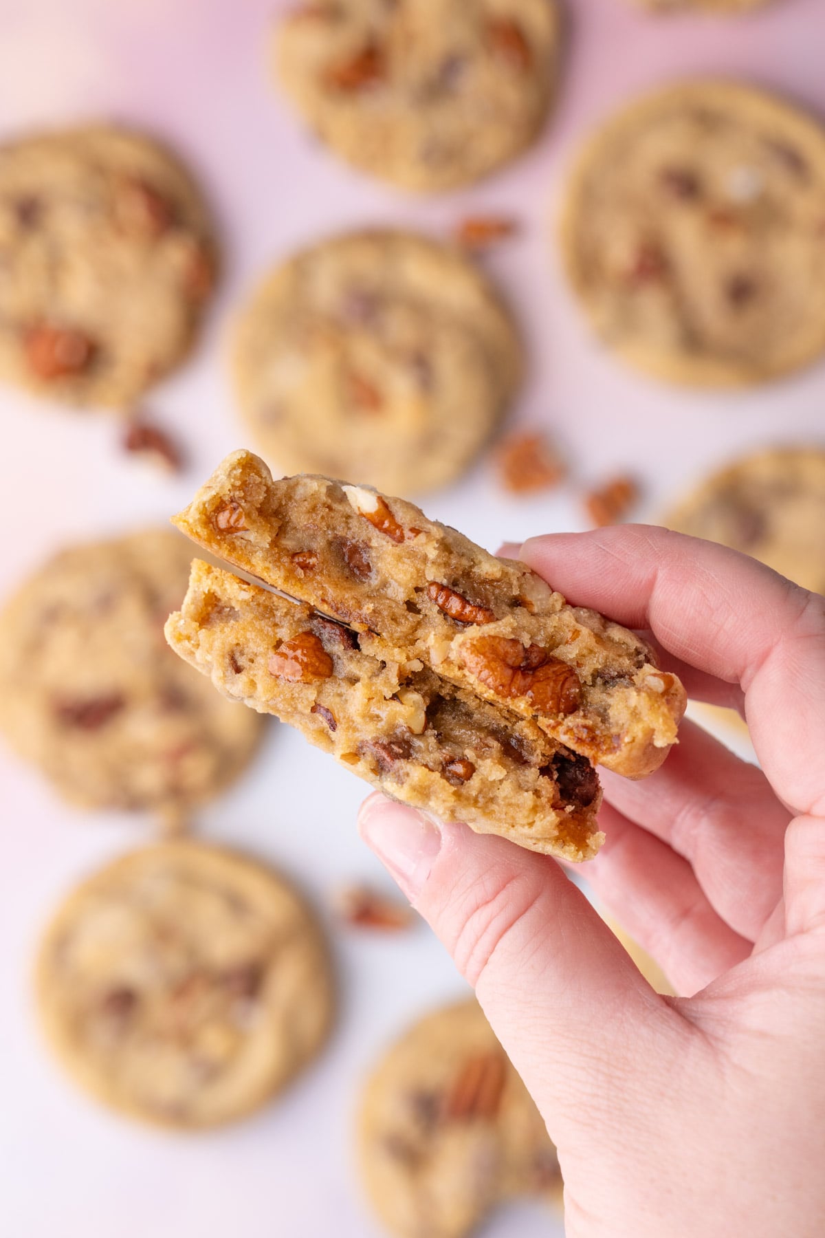 Holding up a cookie thats broken in half to the camera to show the chocolate chips and pecans.