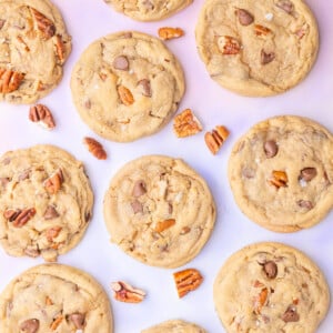 Overhead image of pecan chocolate chip cookies surrounded by pecans on a colorful background.