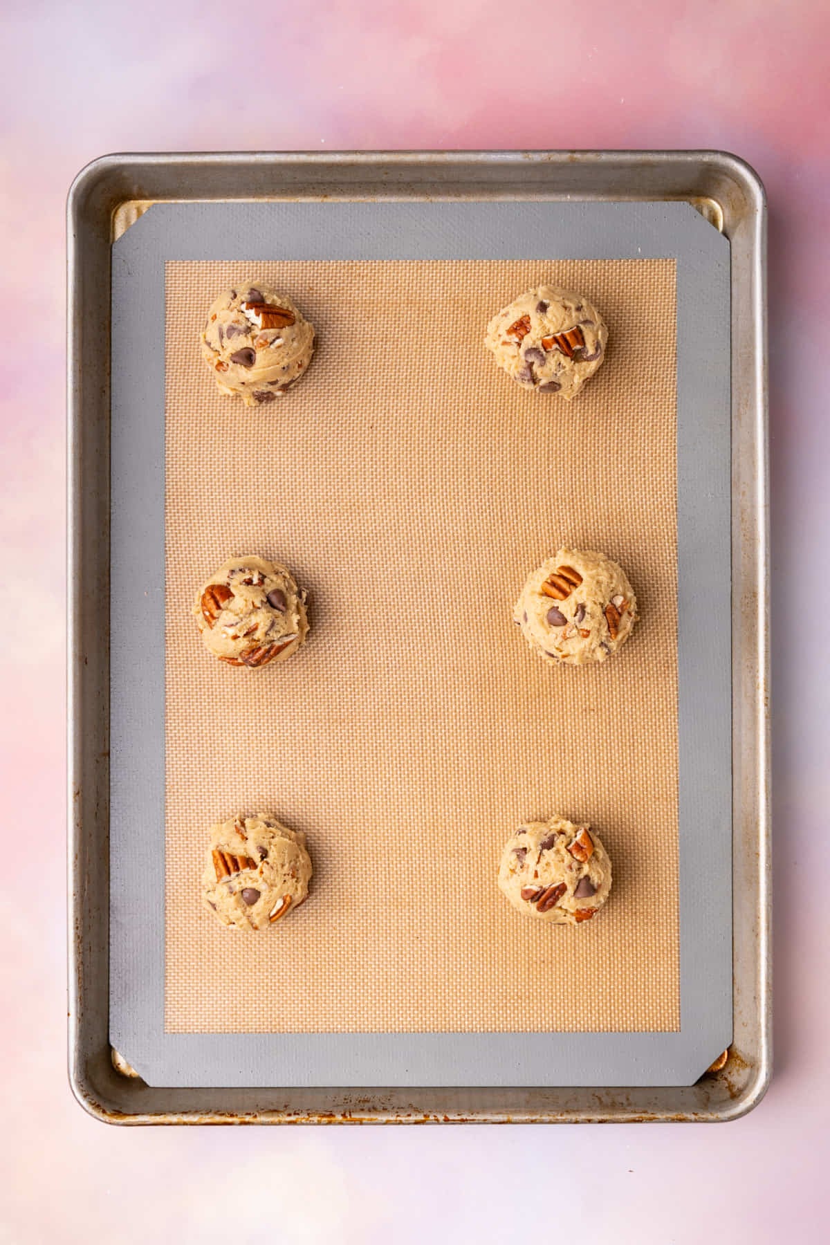 Pecan chocolate chip cookie balls on a lined baking sheet ready to bake in the oven.