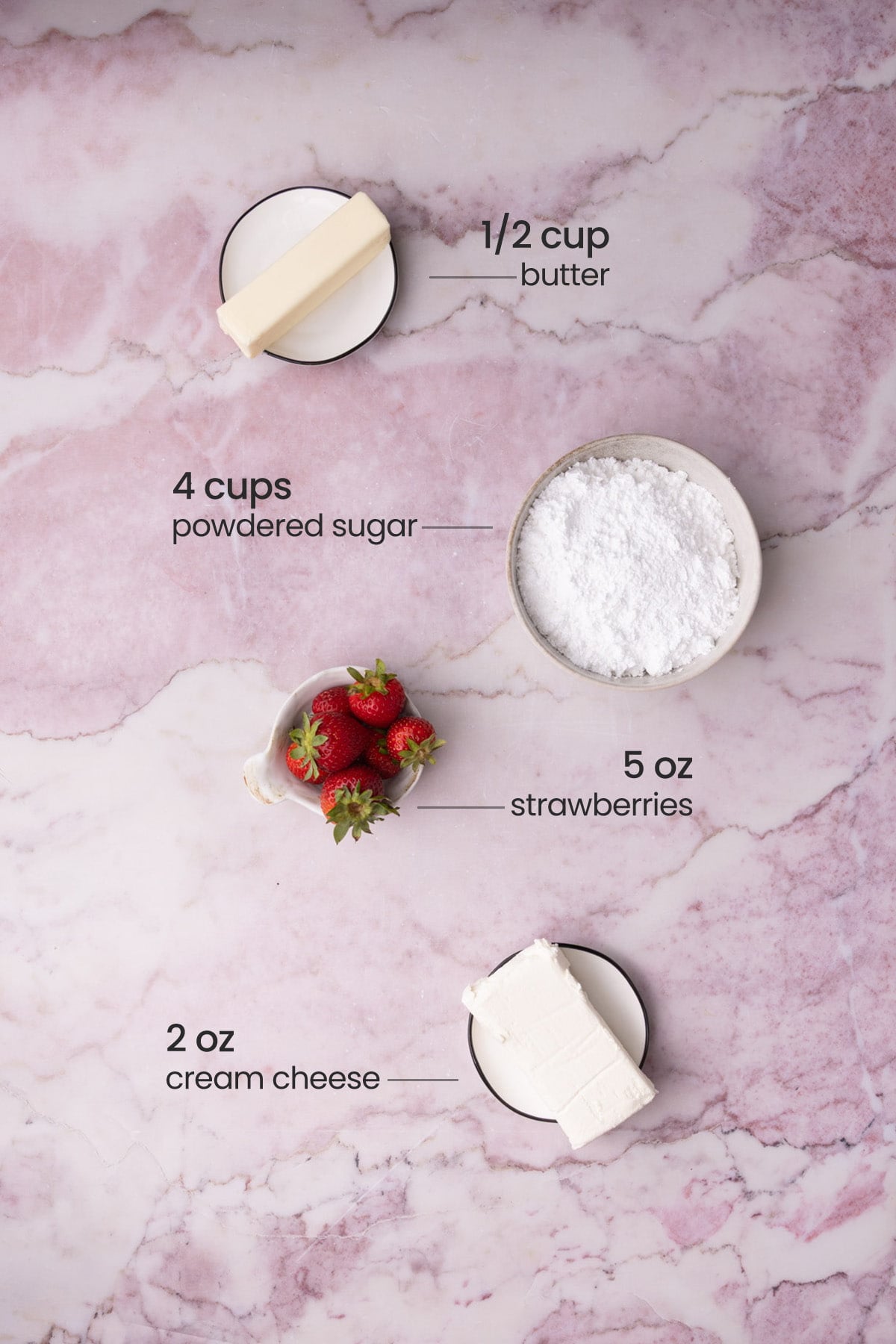 Overhead view of the ingredients for strawberry cream cheese frosting - butter, powdered sugar, strawberries, and cream cheese.