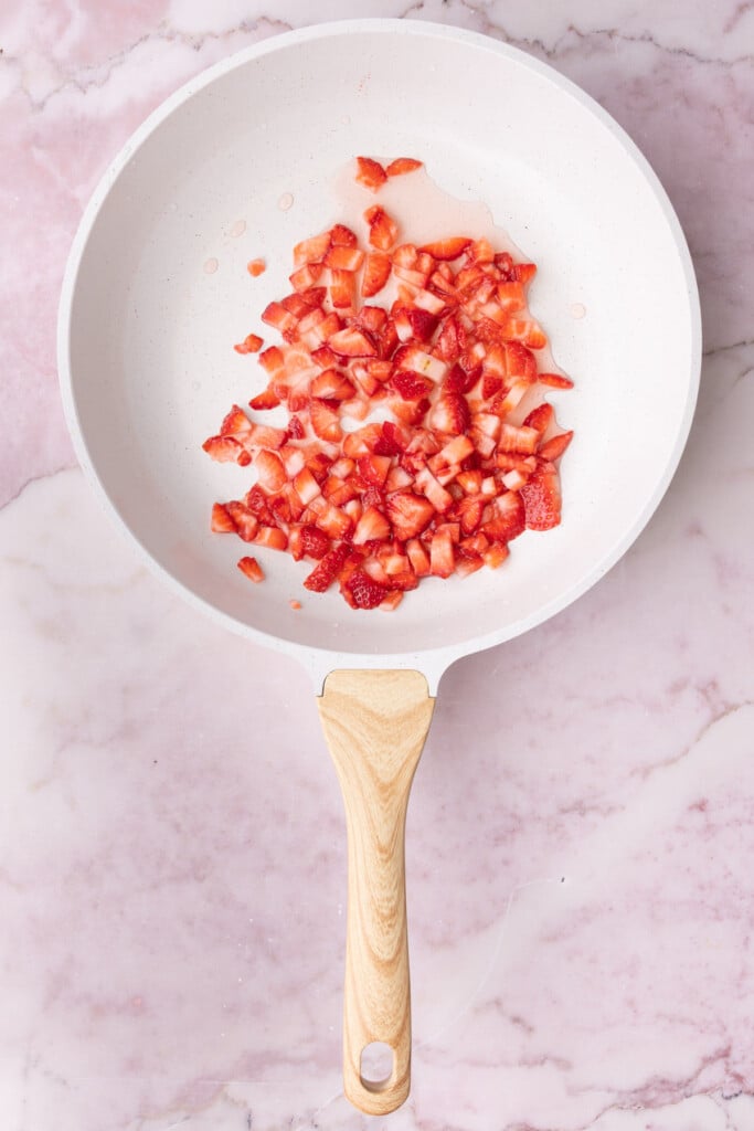 Diced strawberries in a pan over medium heat with water.