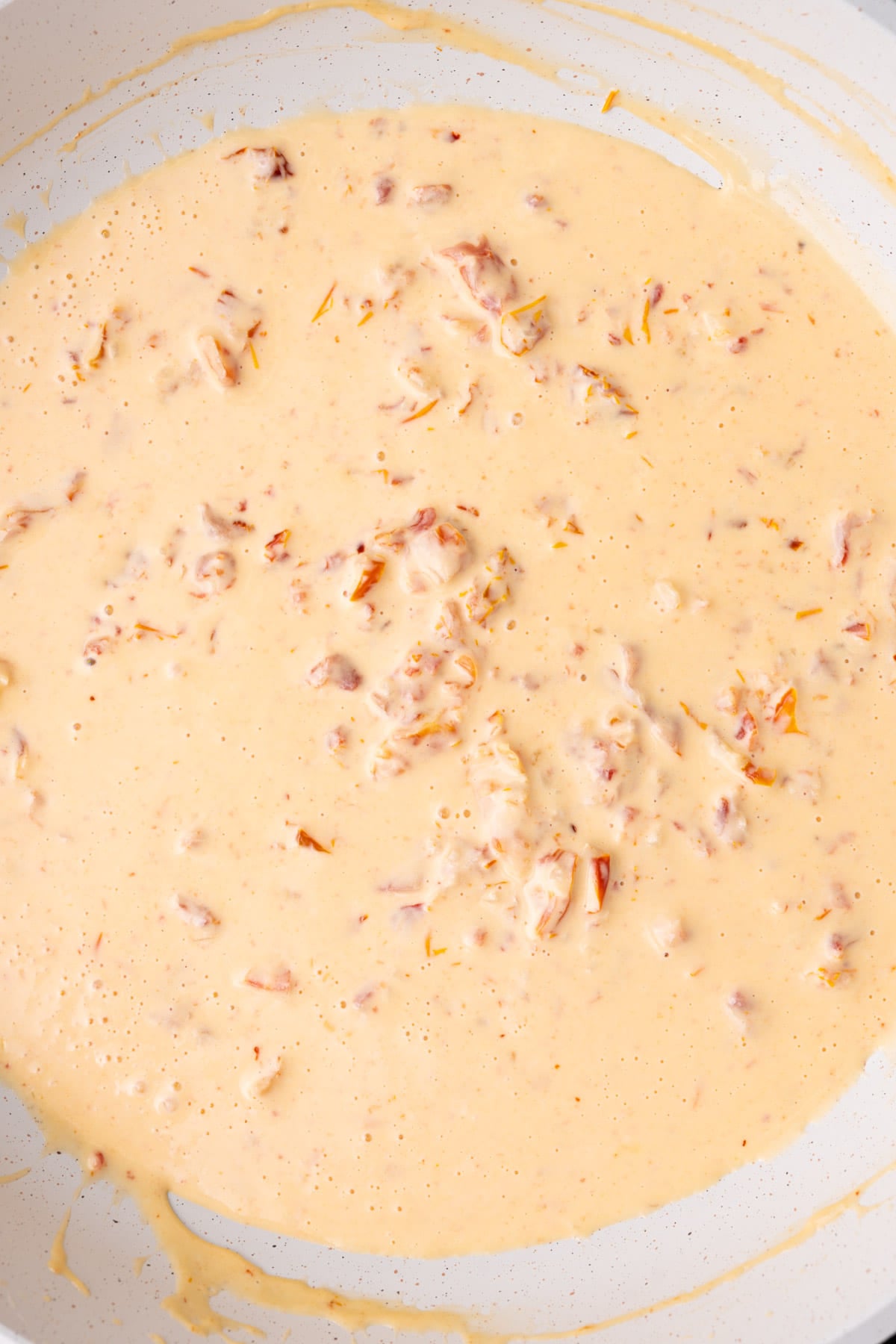 Cream sauce with sun-dried tomatoes and garlic cooking in a pan.