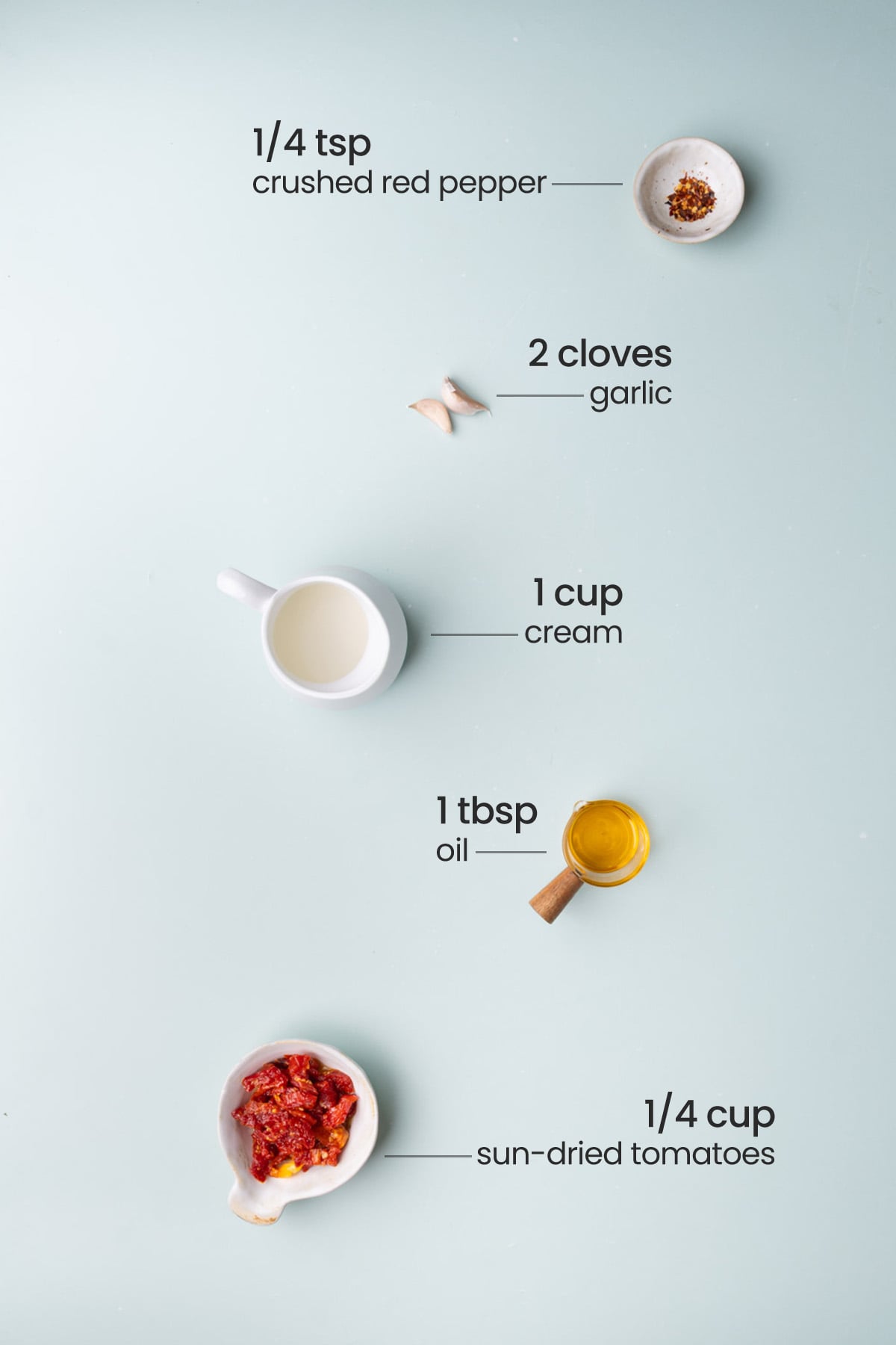Overhead view of all the ingredients for sun-dried tomato cream sauce - crushed red pepper, garlic, cream, oil, and sun-dried tomatoes.