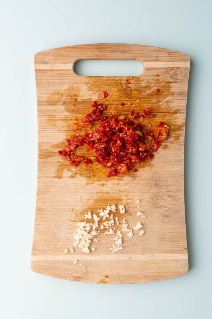 Diced sun-dried tomatoes and minced garlic on a chopping board.
