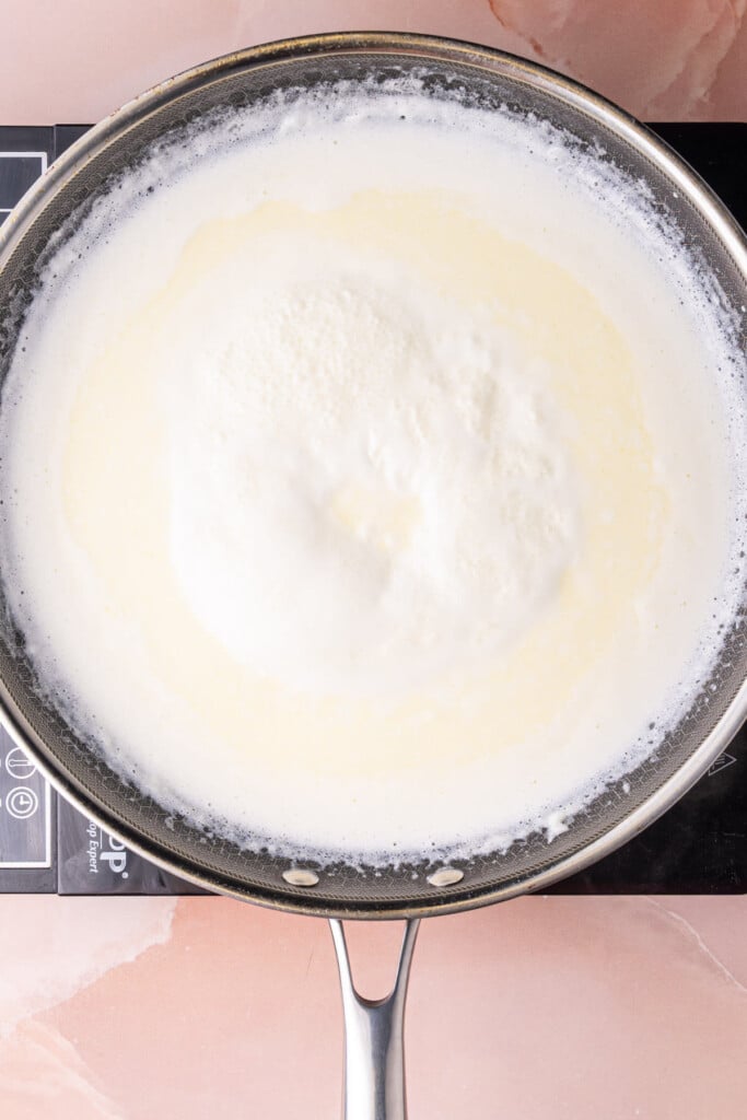 Melting butter into cream and bringing it to a simmer to start to thicken.