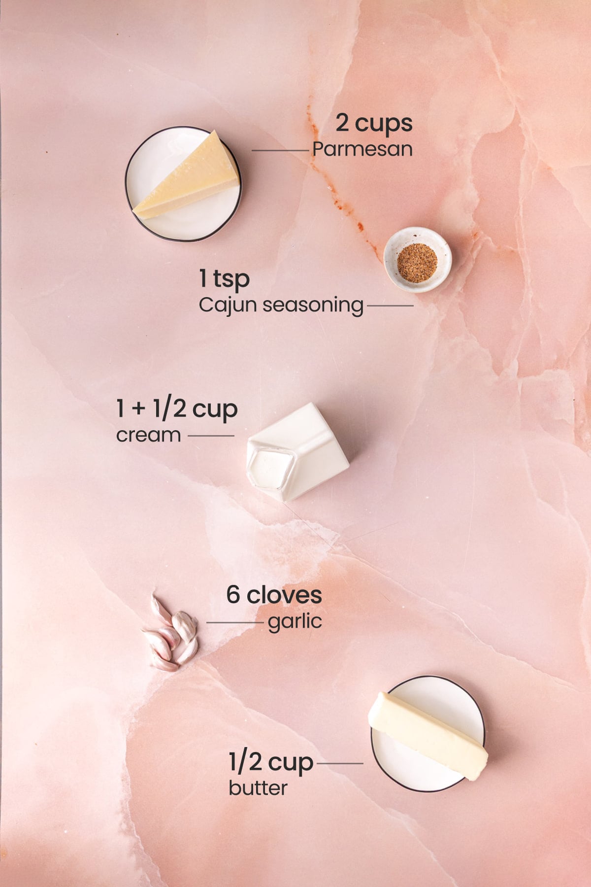 Overhead view of the ingredients for Cajun alfredo sauce - Parmesan, Cajun seasoning, cream, garlic, and butter.