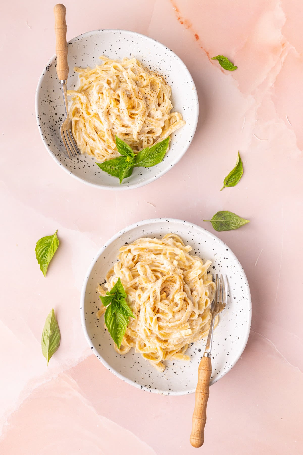 Two bowls of Cajun alfredo sauce with linguine on a pink background.