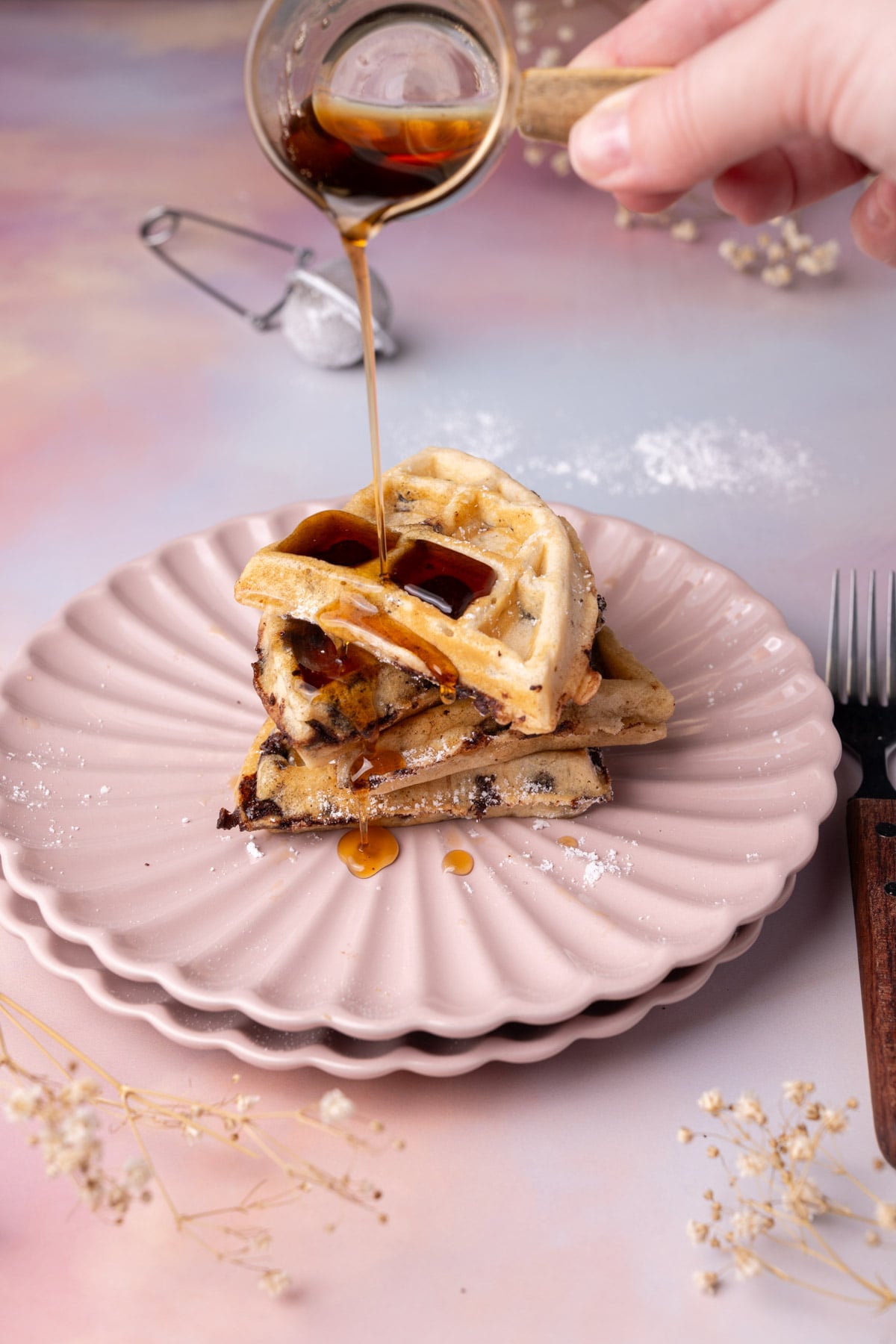 Pouring syrup over 4 quarters of a waffle stacked on top of one another.