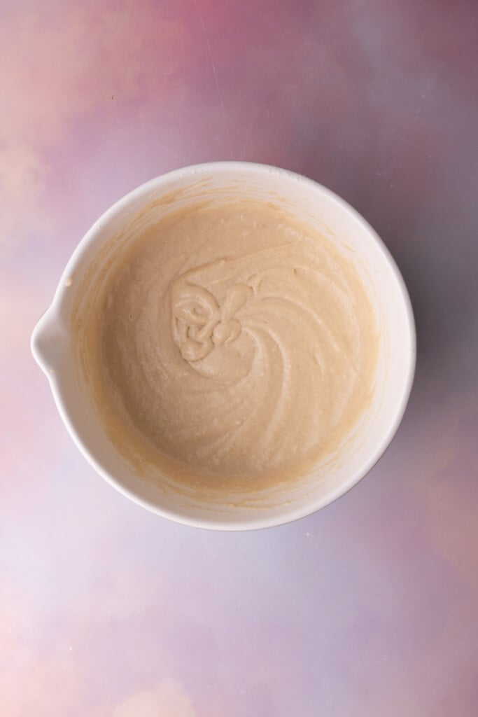 Homemade waffle batter in a mixing bowl on a colorful background.