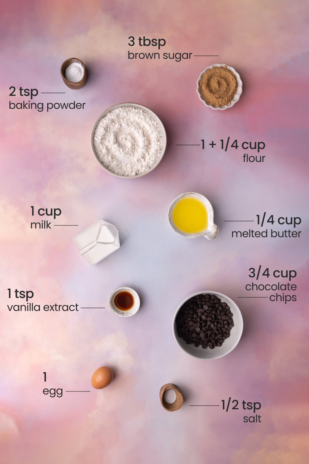 Overhead view of all ingredients needed for chocolate chip waffles - brown sugar, baking powder, flour, milk, melted butter, vanilla extract, chocolate chips, egg, and salt.