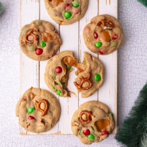 Christmas cookies loaded with green and red M&M's, caramel, and pretzels on a white board.