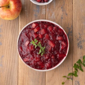 Overhead image of a bowl of vibrant homemade cranberry sauce with apples garnished with fresh thyme.