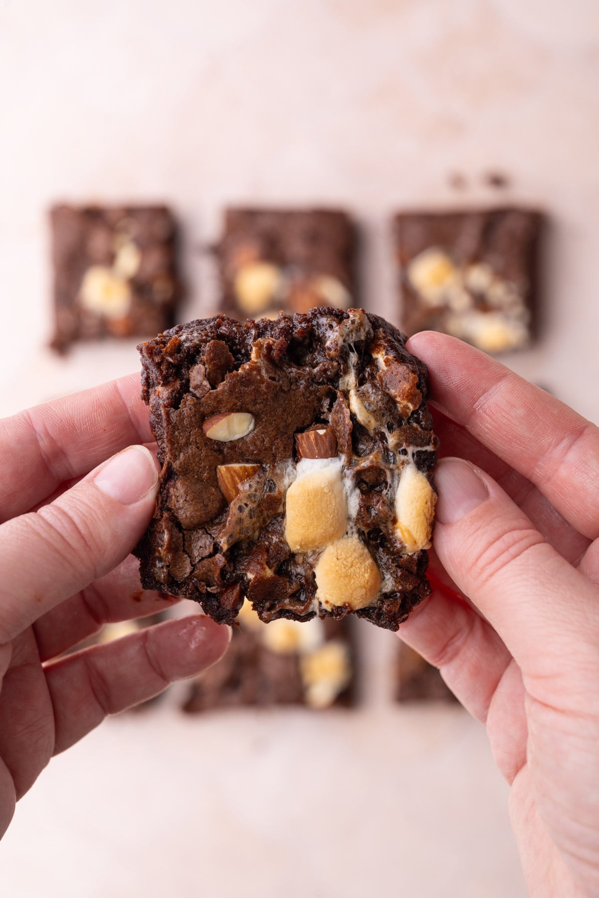 Holding a Rocky Road Brownie up to the camera to see a close up of the toasted marshmallows and bits of almond on top and inside the brownie.