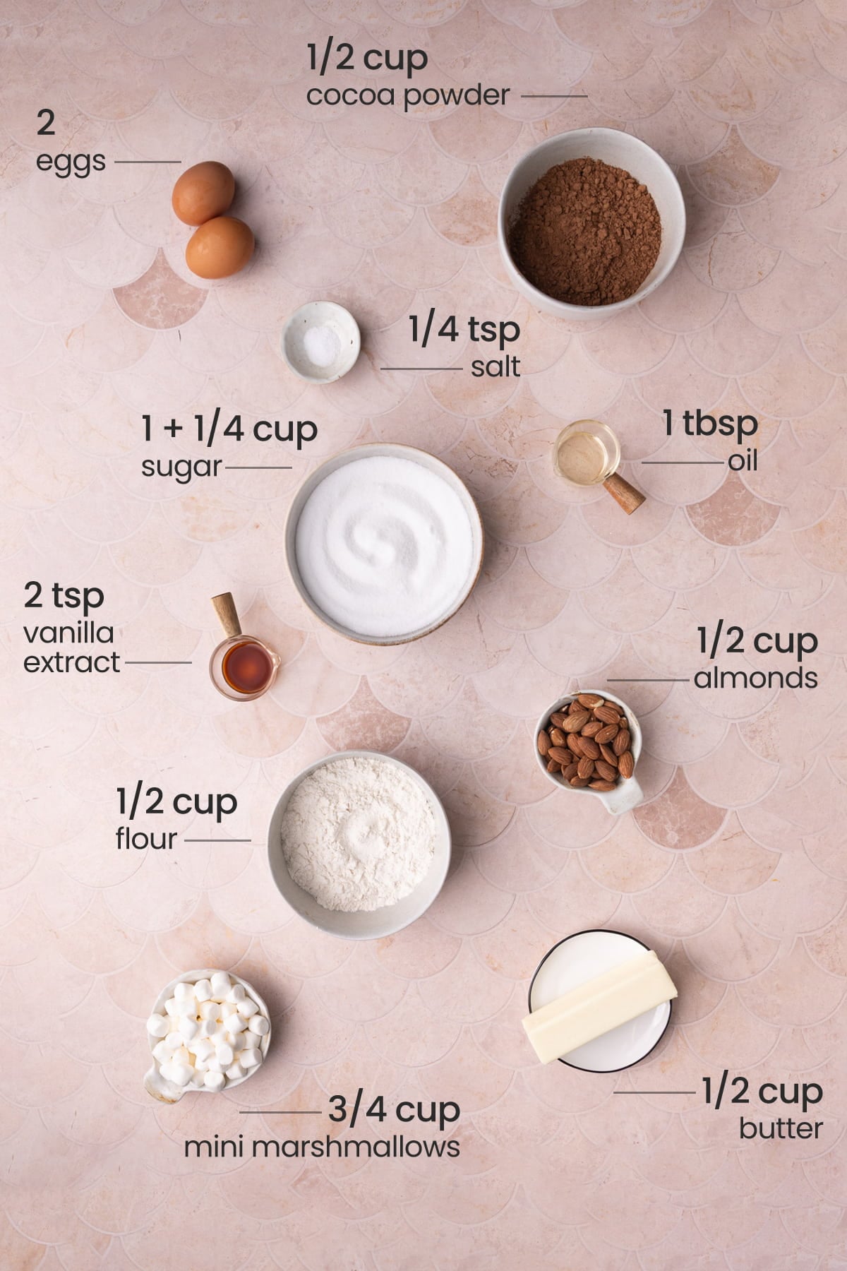 All ingredients needed for Rocky Road brownies including eggs, cocoa powder, salt, flour, oil, vanilla extract, sugar, almonds, butter, and marshmallows.