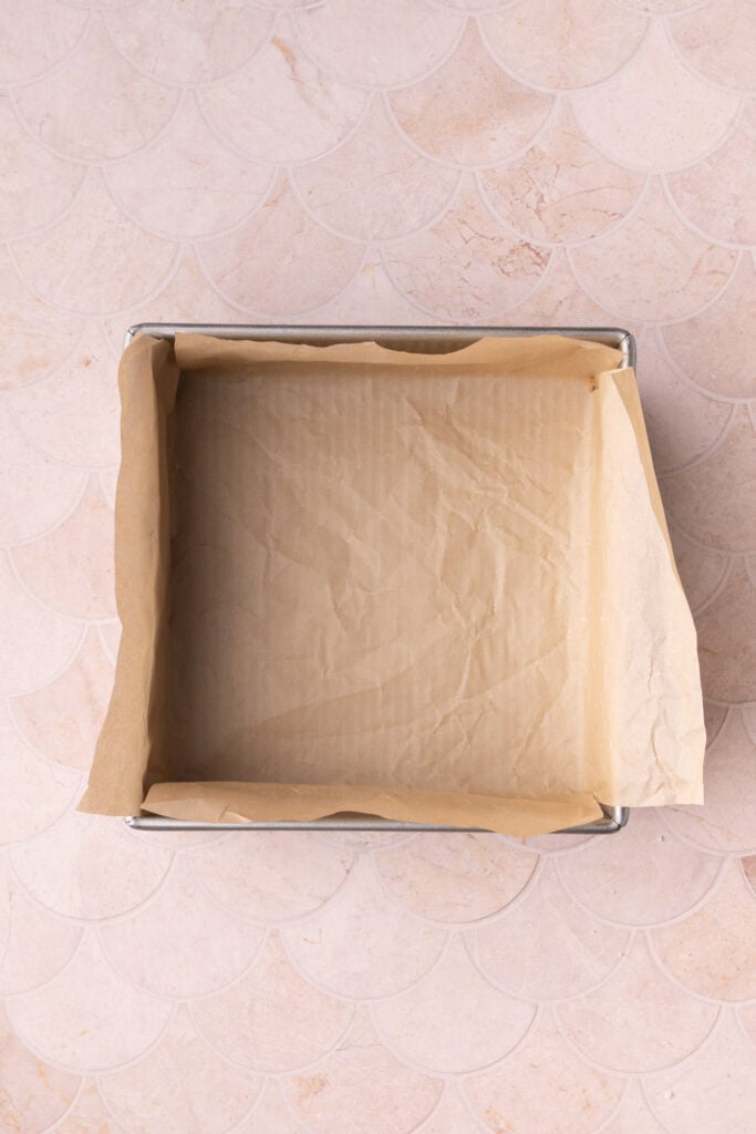 Brownie pan lined with parchment paper with pieces up the side to help easily lift the brownies out once baked.