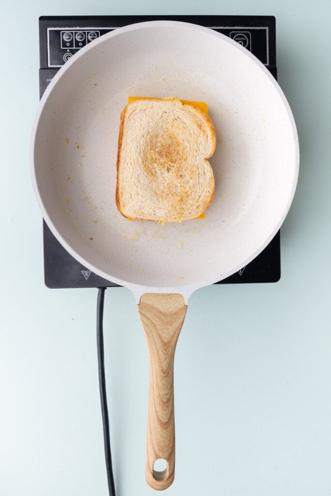Assembling scrambled egg sandwich in a pan.
