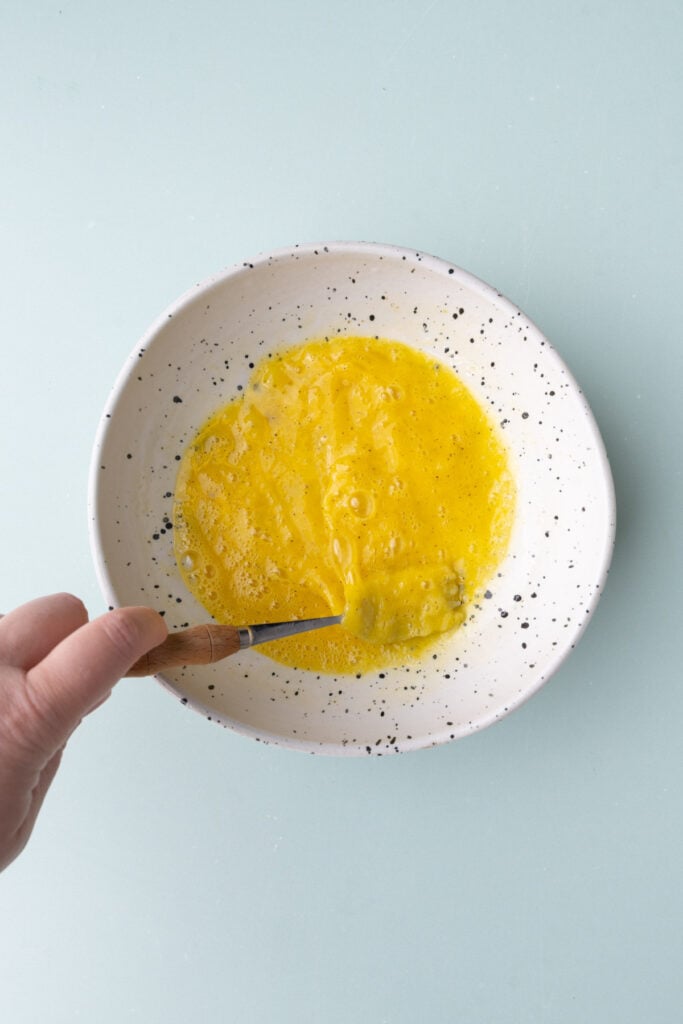 Eggs, salt, and pepper being whisked with a fork to make scrambled eggs.