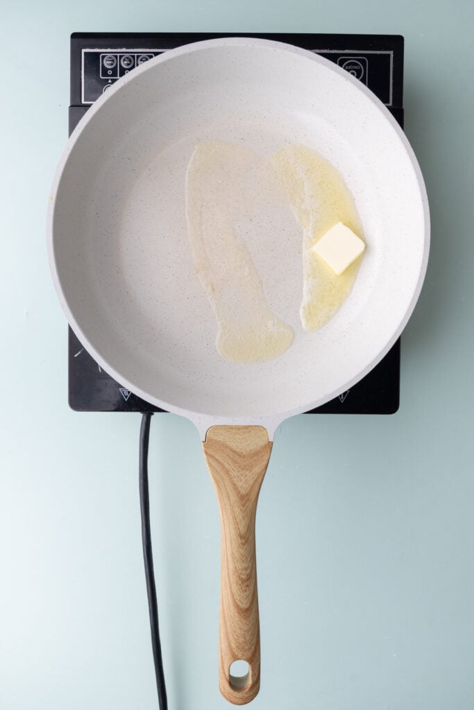Butter melting in a white frying pan.