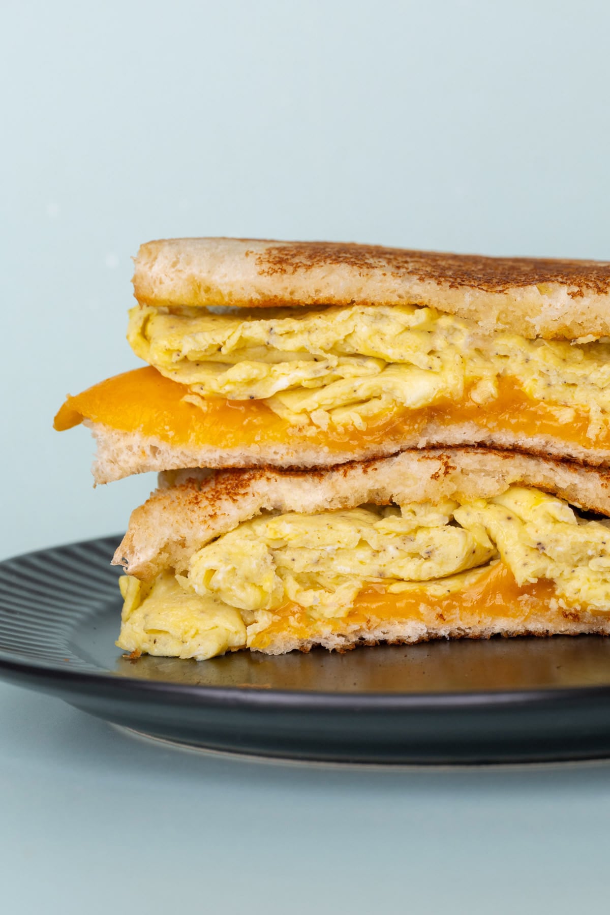Close up cropped photo of breakfast sandwich with scrambled egg and cheese cut in half and stacked on top of one another.