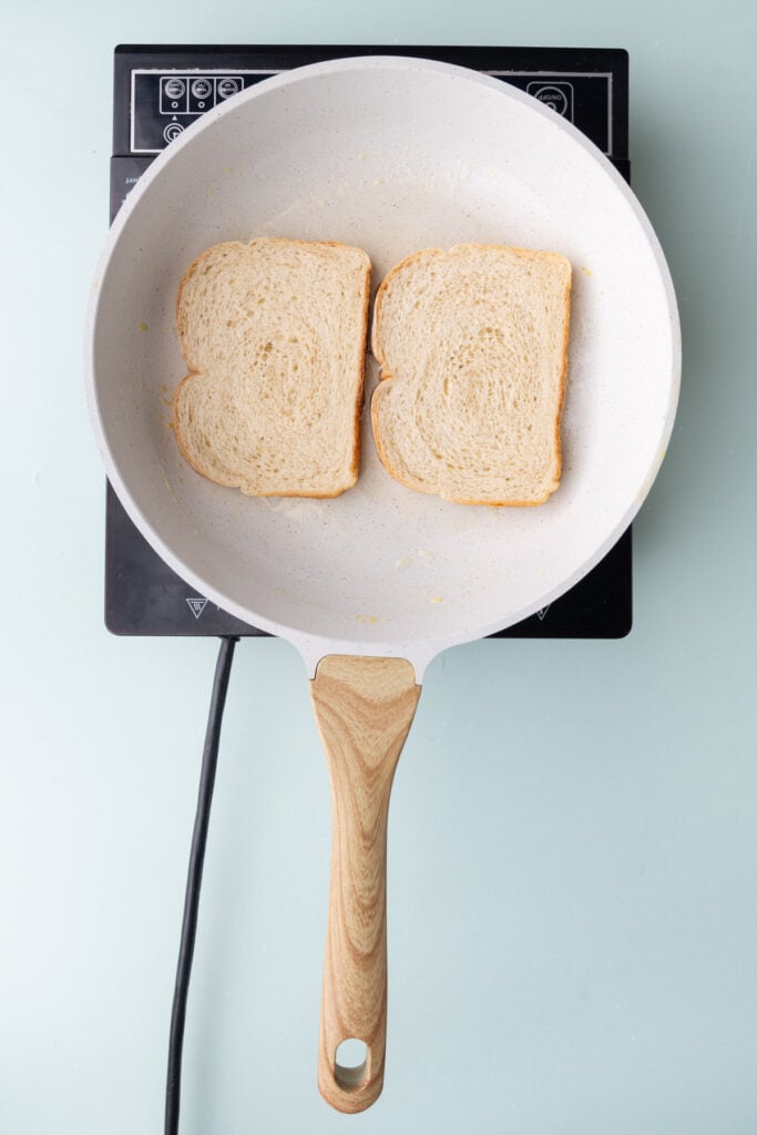 Two slices of bread toasting in a pan with butter.