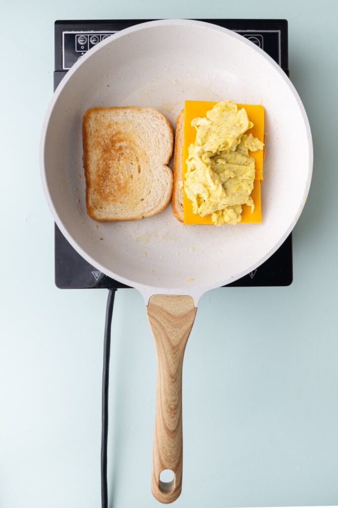 Stacking cheese and scrambled eggs on toasted bread.