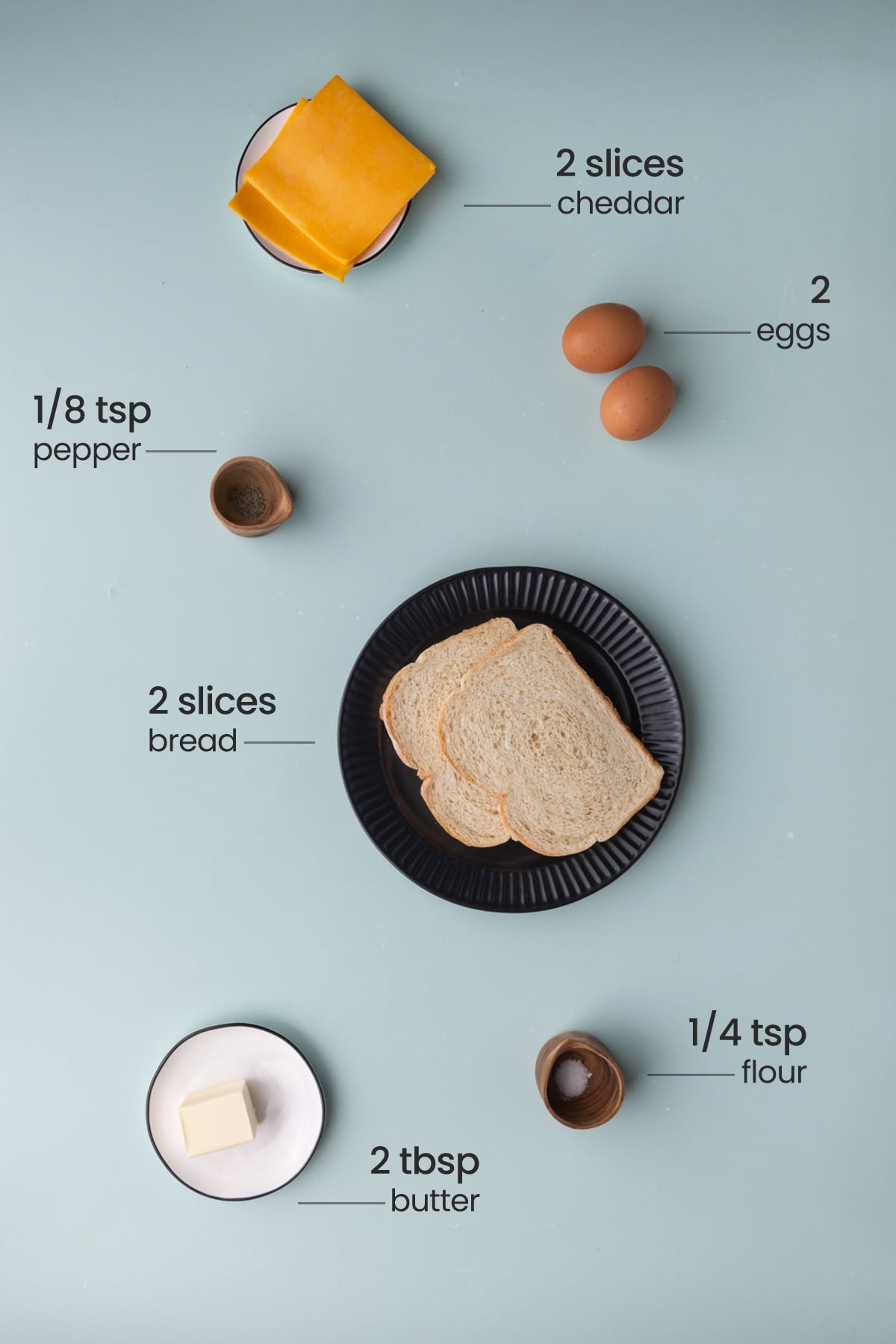 All ingredients needed for a scrambled egg sandwich including cheese, eggs, pepper, bread, salt, and butter.