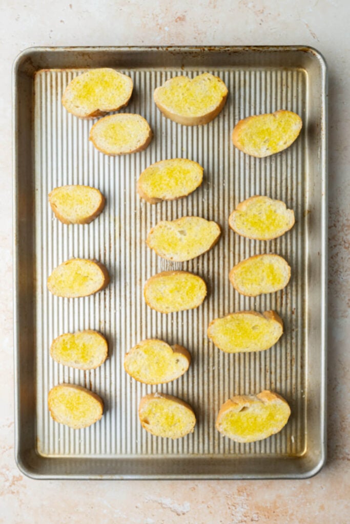 Sliced baguette brushed with olive oil on both sides to toast in the oven for bruschetta.