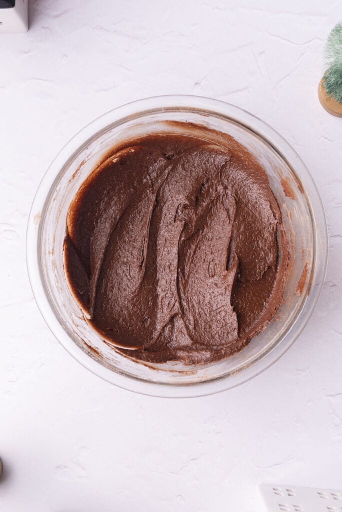 Fluffy and thick brownie batter in a glass mixing bowl.