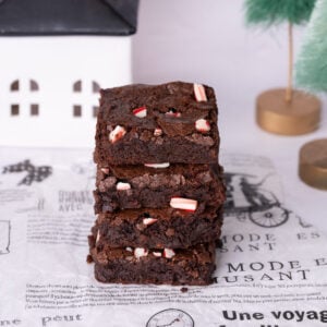 Candy cane brownies stacked up on top of one another with a Christmas scene in the background.