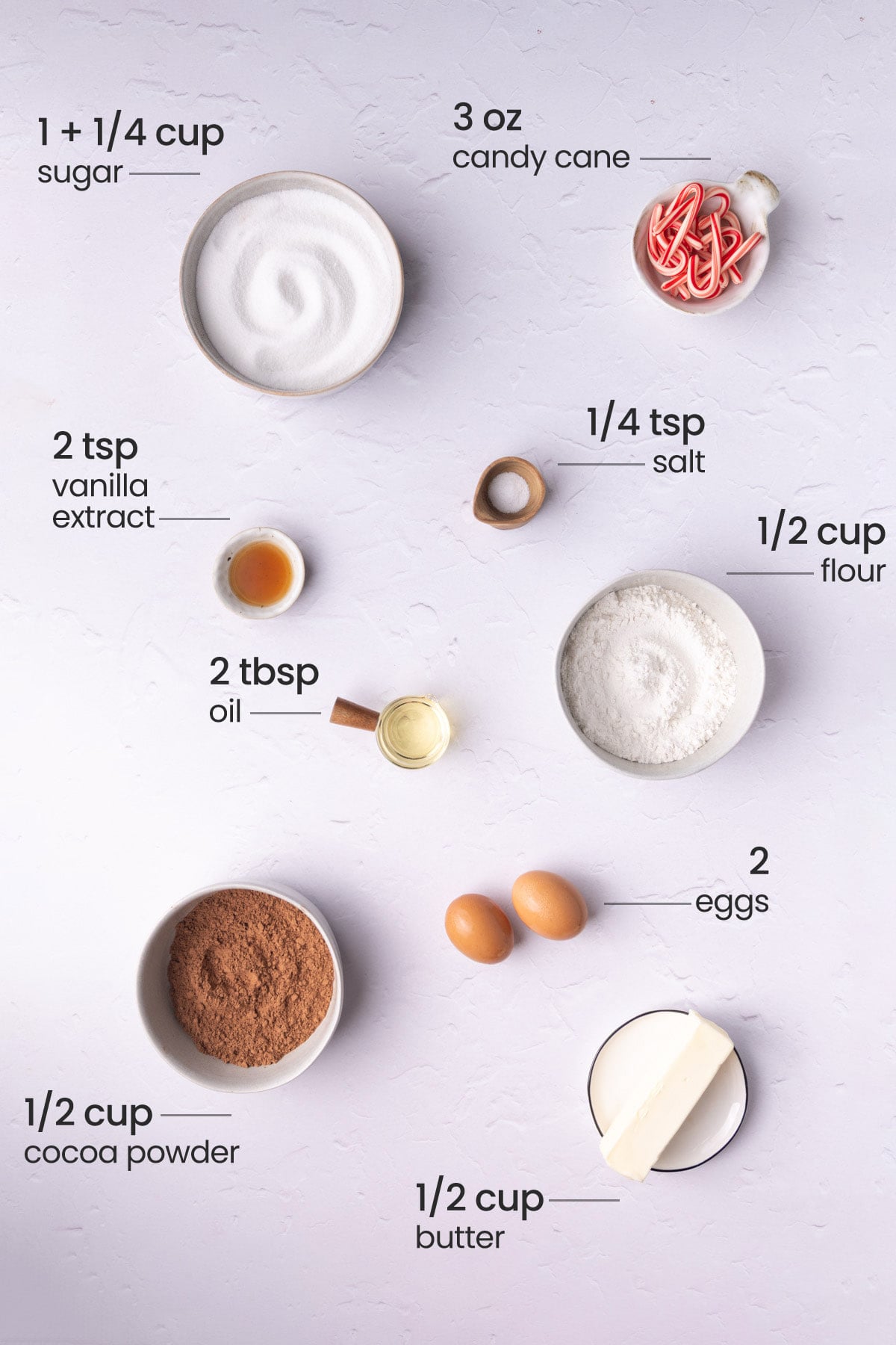 All the ingredients needed to make candy cane brownies including sugar, candy cane, salt, vanilla extract, all-purpose flour, oil, eggs, cocoa powder, and butter.