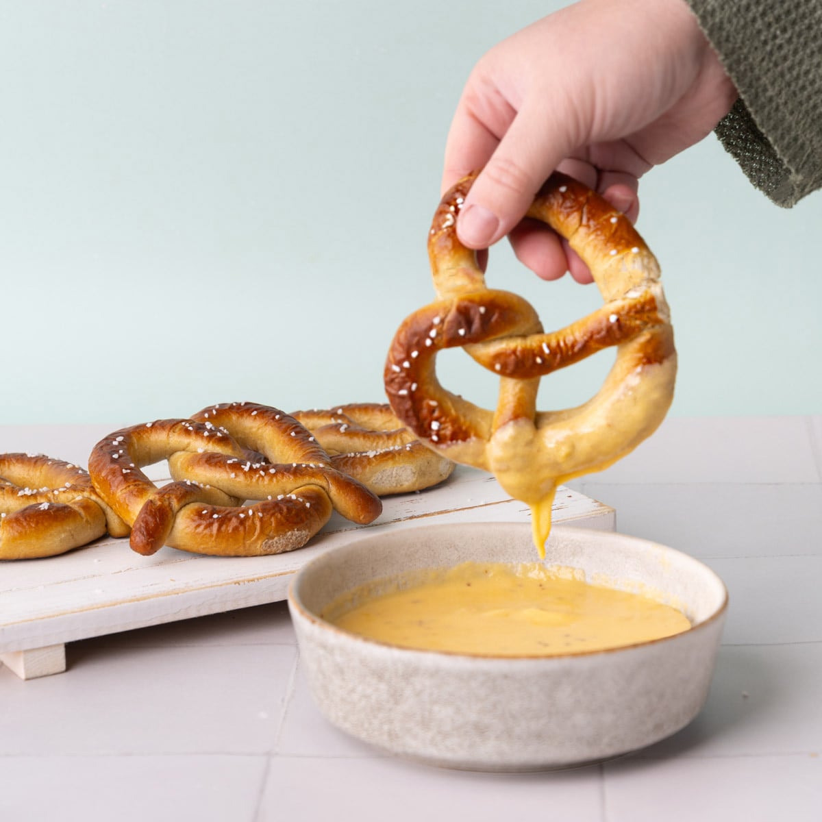 Cheese dipping sauce for pretzels in a small bowl with a pretzel dunked in and the cheese sauce dripping off.