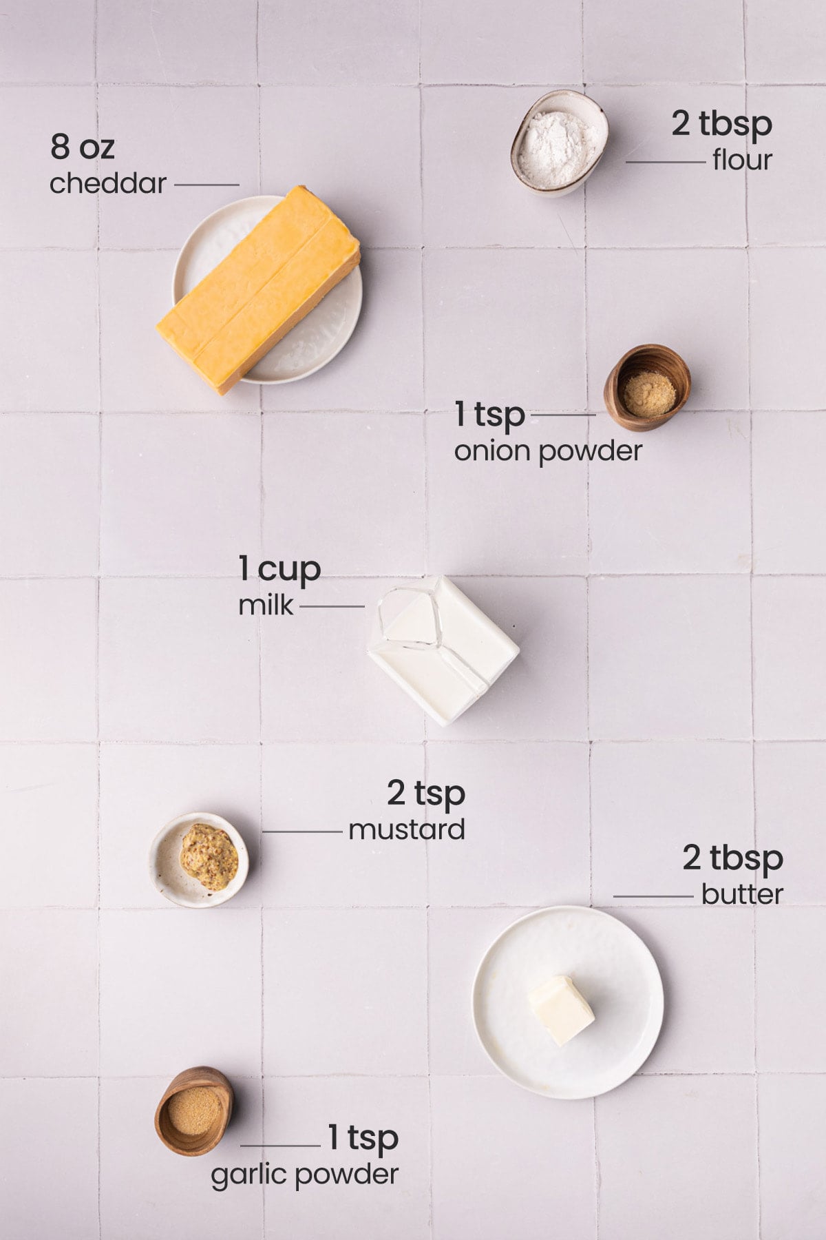 Overhead view of the ingredients needed for cheese sauce for pretzels - cheddar, flour, onion powder, milk, mustard, butter, and garlic powder.