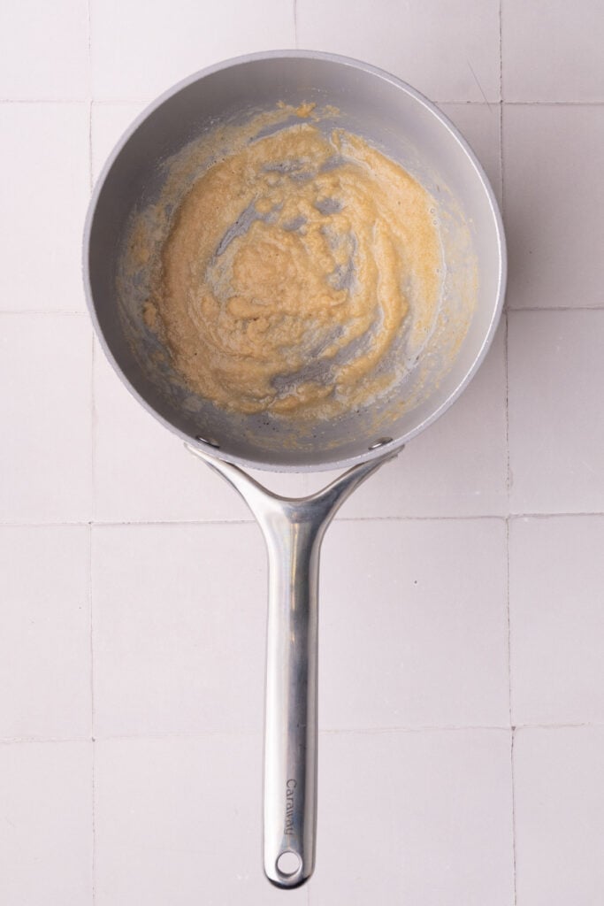 Butter, flour, and seasonings mixed together in a small pot to form a roux to make a creamy cheddar cheese sauce.