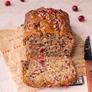Loaf of cranberry banana bread with one slice open to show top and inside textures of the bread.