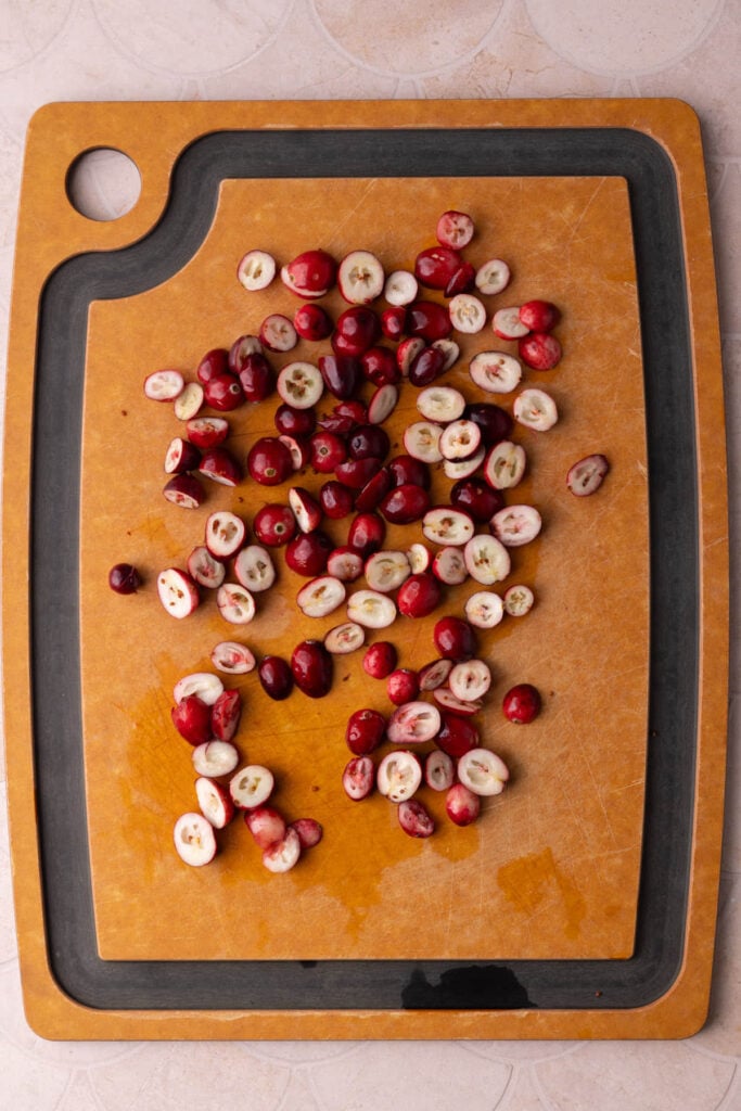 Fresh cranberries on a chopping board sliced in half so they can be diced without rolling away.
