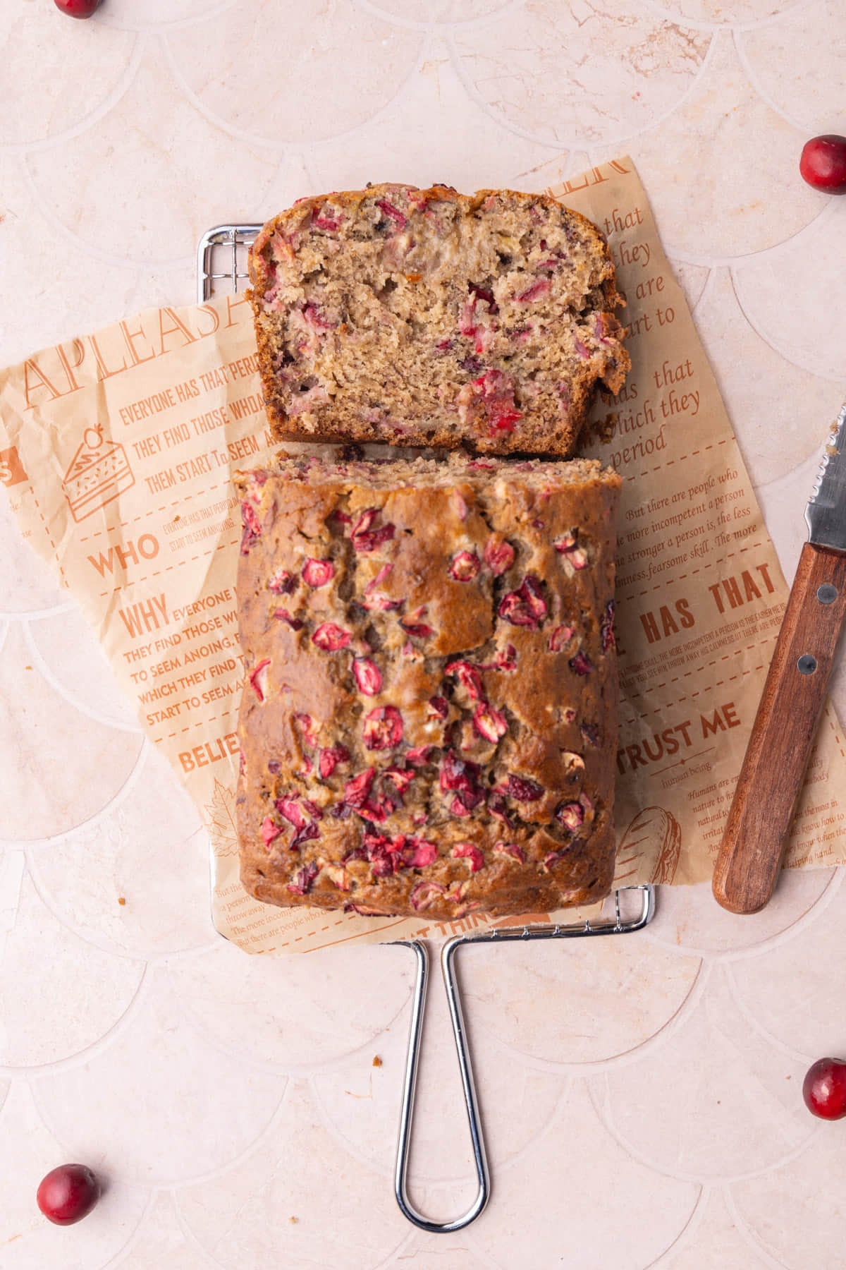 Overhead image of banana bread with fresh cranberries with one slice laying on its side to show the texture of the inside of the bread.