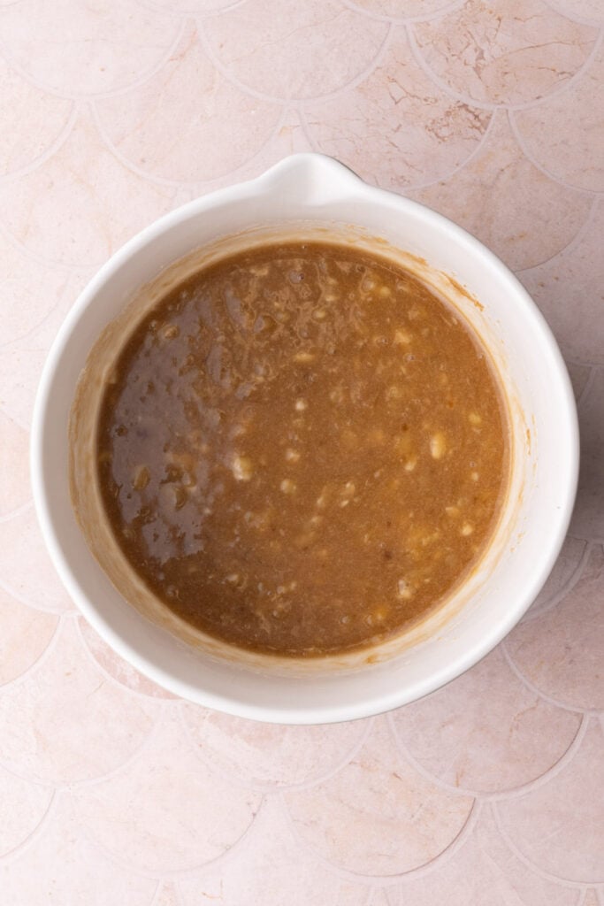 Brown sugar and oil mixed with mashed banana in a mixing bowl.
