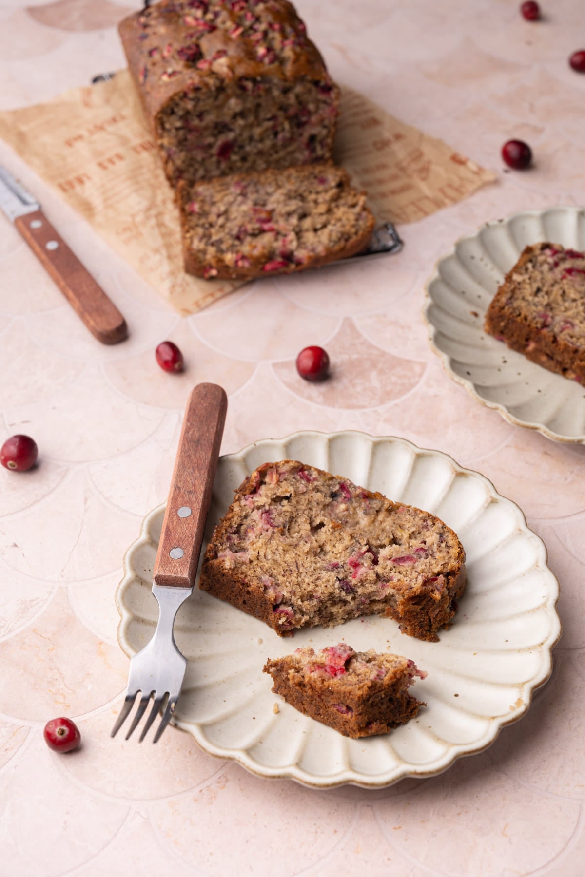 Slice of cranberry banana bread on a plate, with a wooden fork.