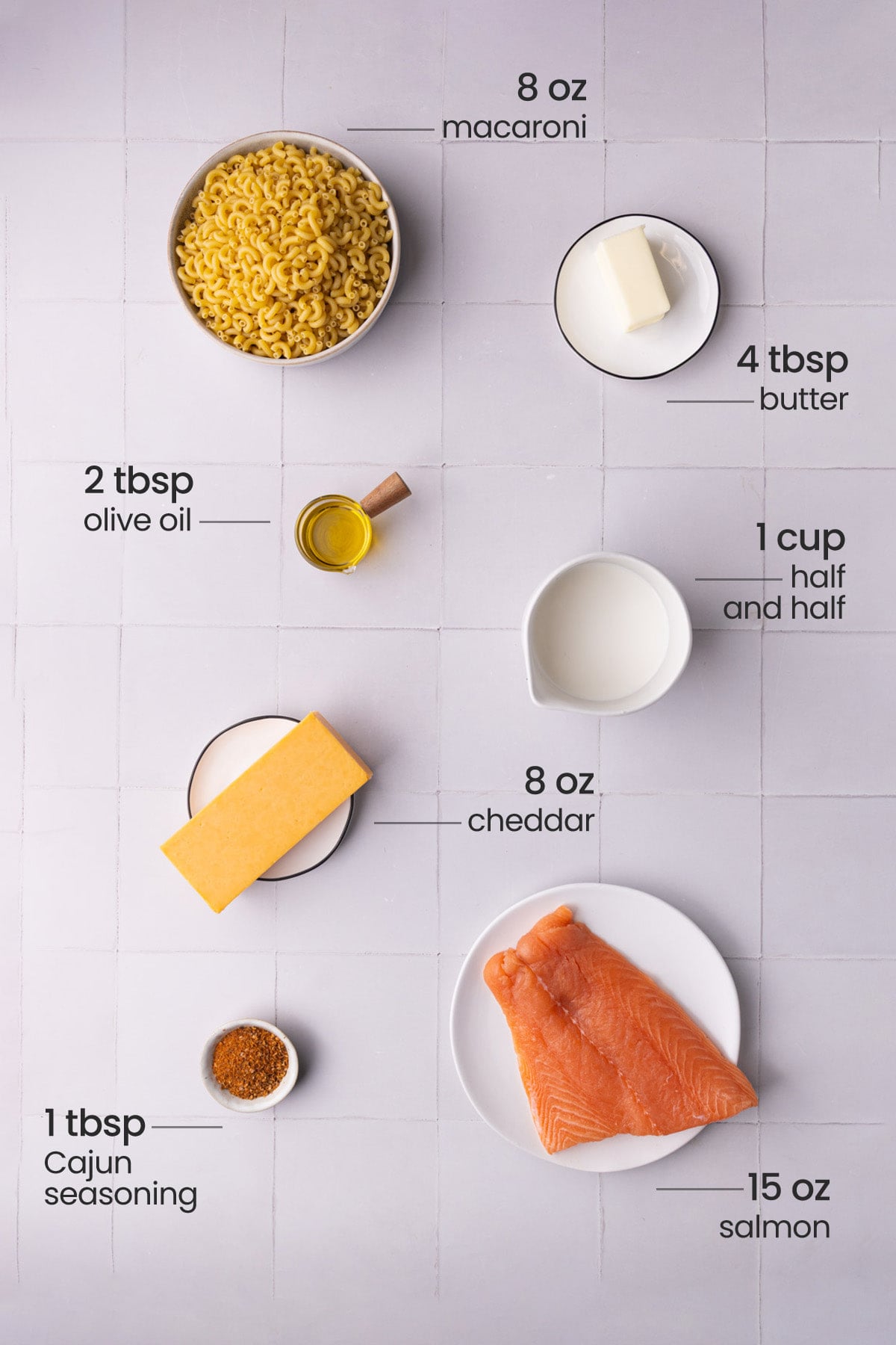 Overhead view of all the ingredients needed for salmon man and cheese - macaroni, butter, olive oil, half and half, cheddar, Cajun seasoning, and salmon.