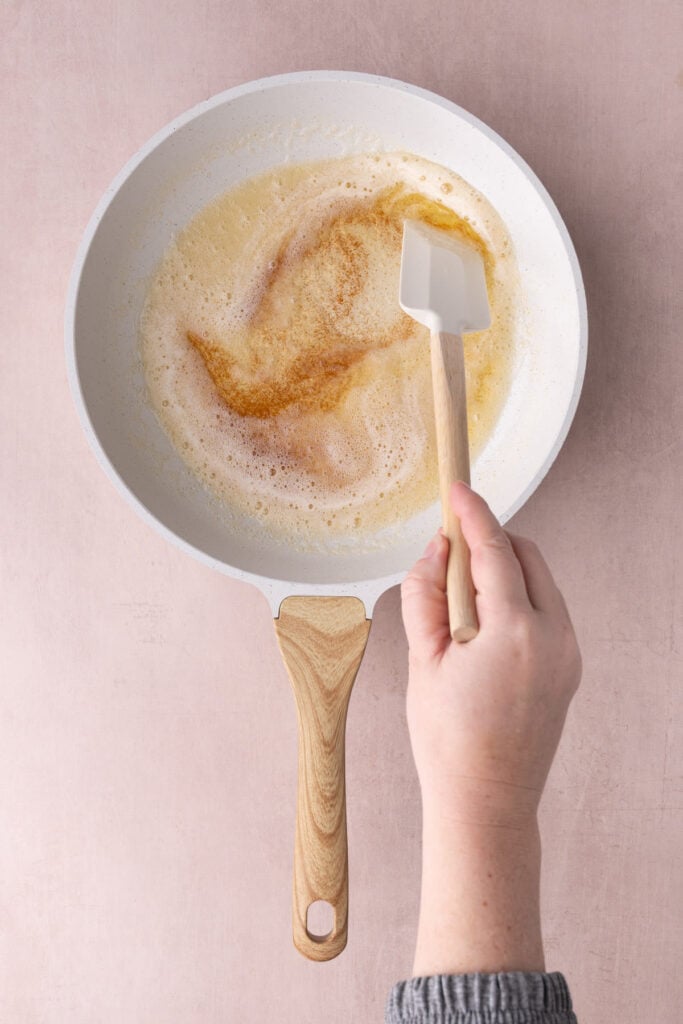 Butter browning in a white pan being stirred with a rubber spatula.