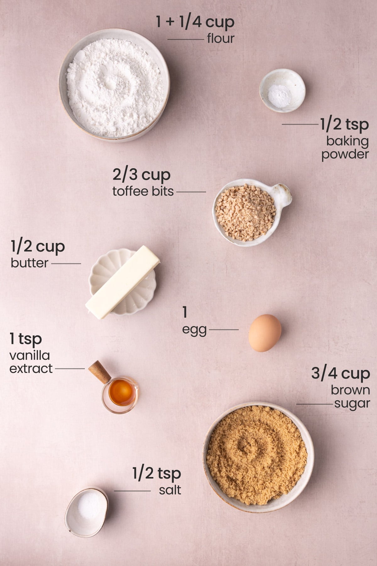 Overhead view of the ingredients needed for butter crunch cookies - flour, baking powder, toffee bits, butter, egg, vanilla extract, brown sugar, and salt.